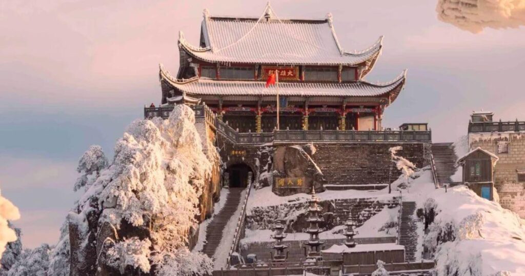 九華山冬季被白雪覆蓋的寺廟,古色古香的屋簷與台階映襯在粉色晚霞下,景色莊嚴而浪漫。